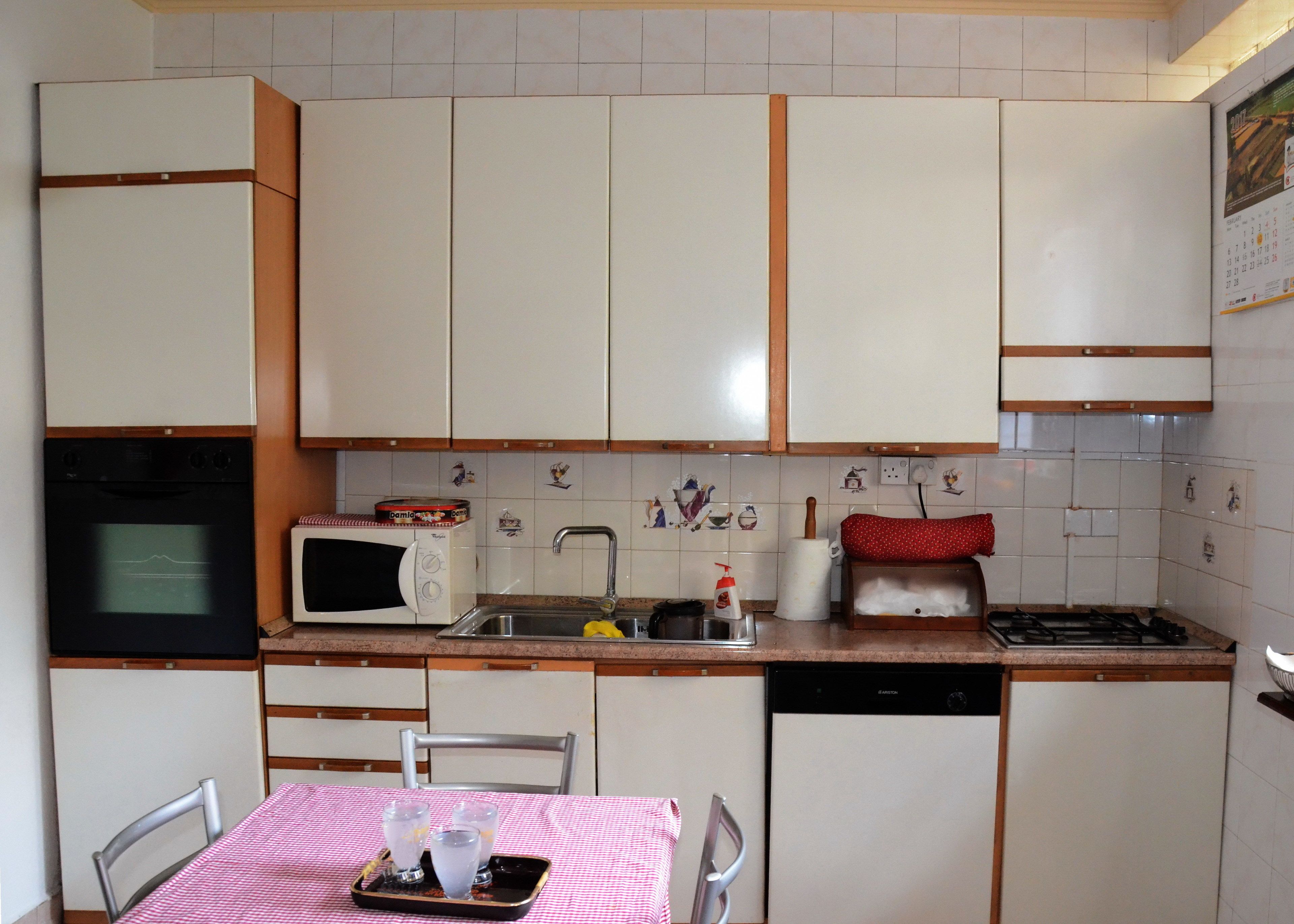 A compact kitchen with white cabinets, a microwave, a stove, and a sink. There is a table with a checkered tablecloth and glasses.