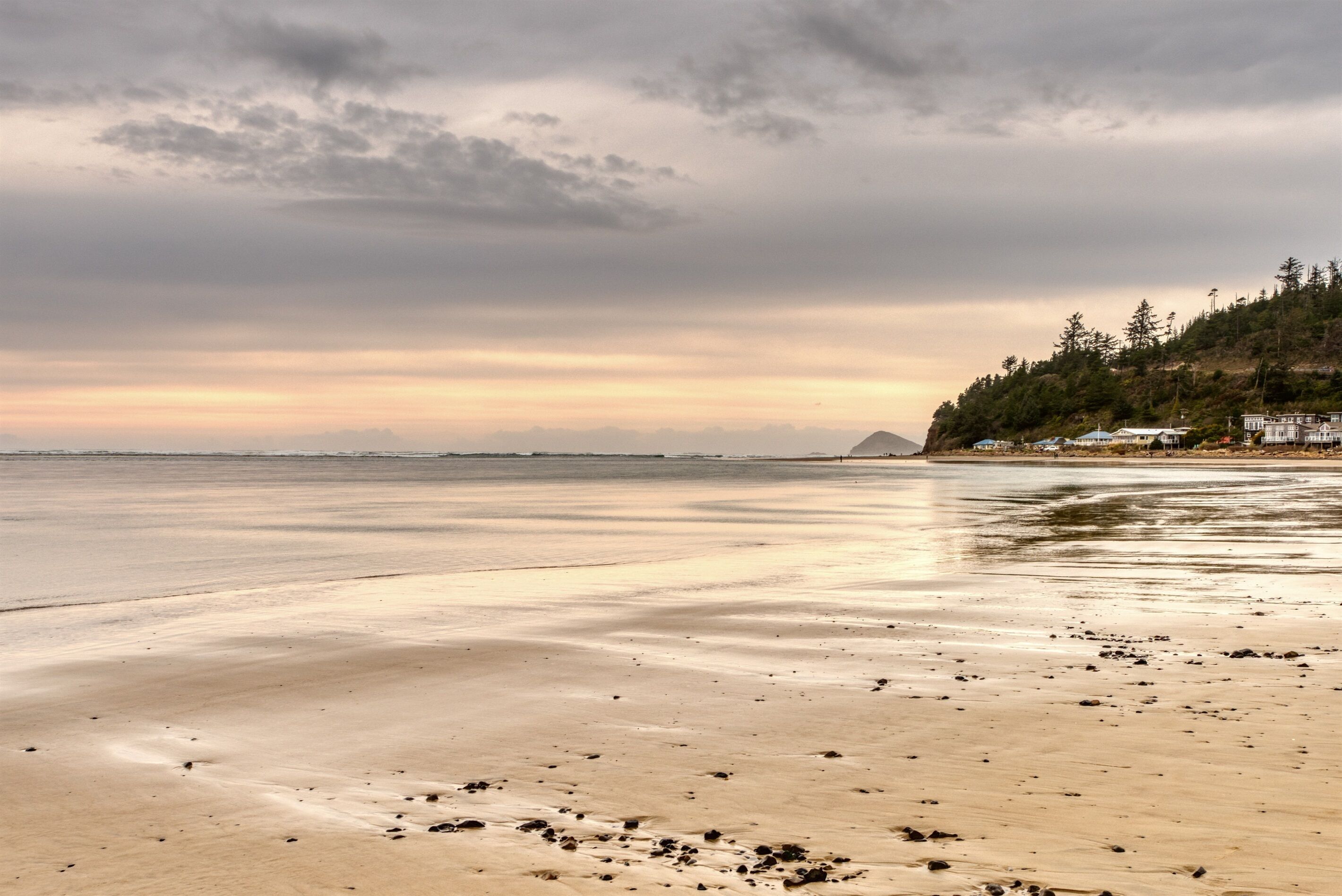 Uma praia com mar calmo, areal arenoso e uma colina arborizada ao fundo.