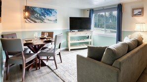 A living room with a dining area, a flat-screen TV, and a large window with curtains.