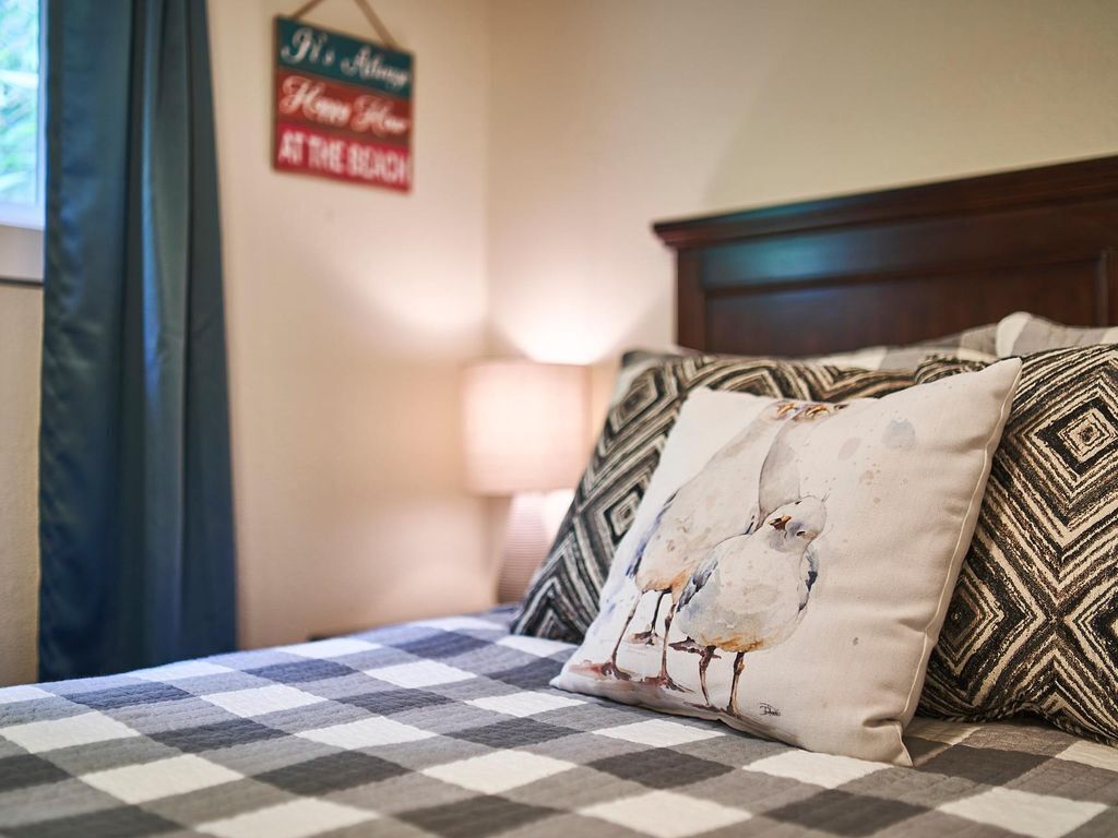 Ein Bett mit kariertem Überwurf, ein Kopfkissen mit Vogelmotiv und ein Wandschild.