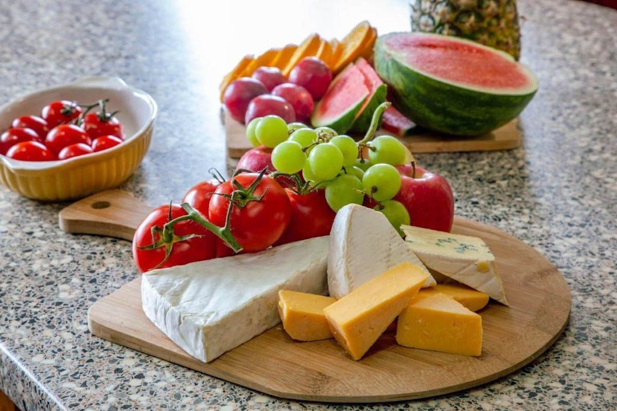 Una tabla de quesos con varios tipos de queso, uvas, tomates y una tajada de sandía.