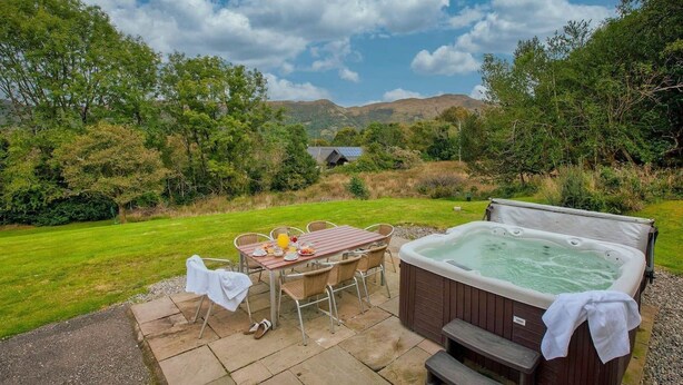 A hot tub and dining area with a view of hills and trees.