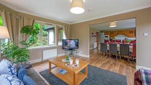 A living room with a TV, sofa, coffee table, and a view of the kitchen.