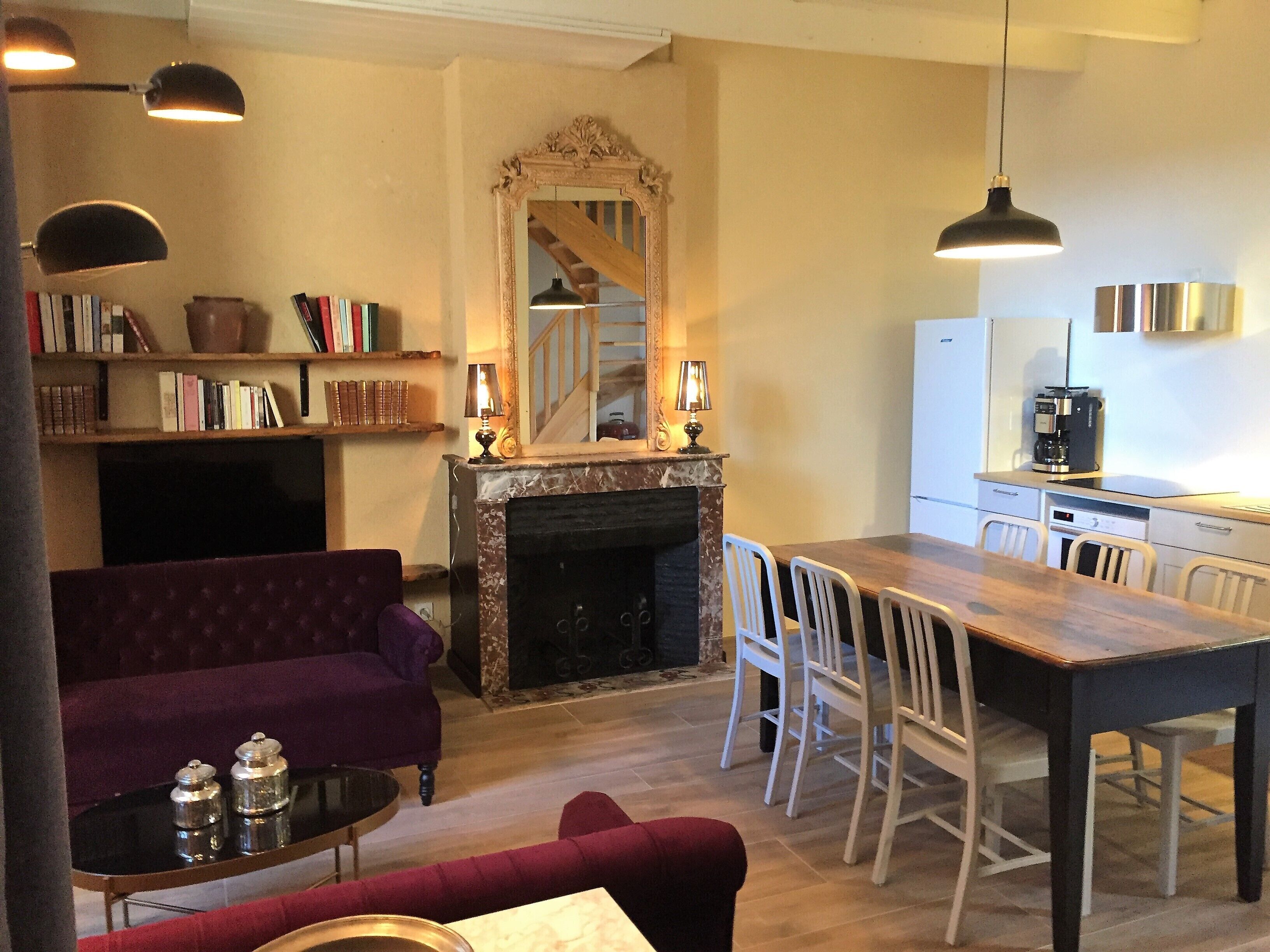 Een gezellige woonkamer met een open haard, een eettafel met stoelen, een paarse bank en een boekenkast.