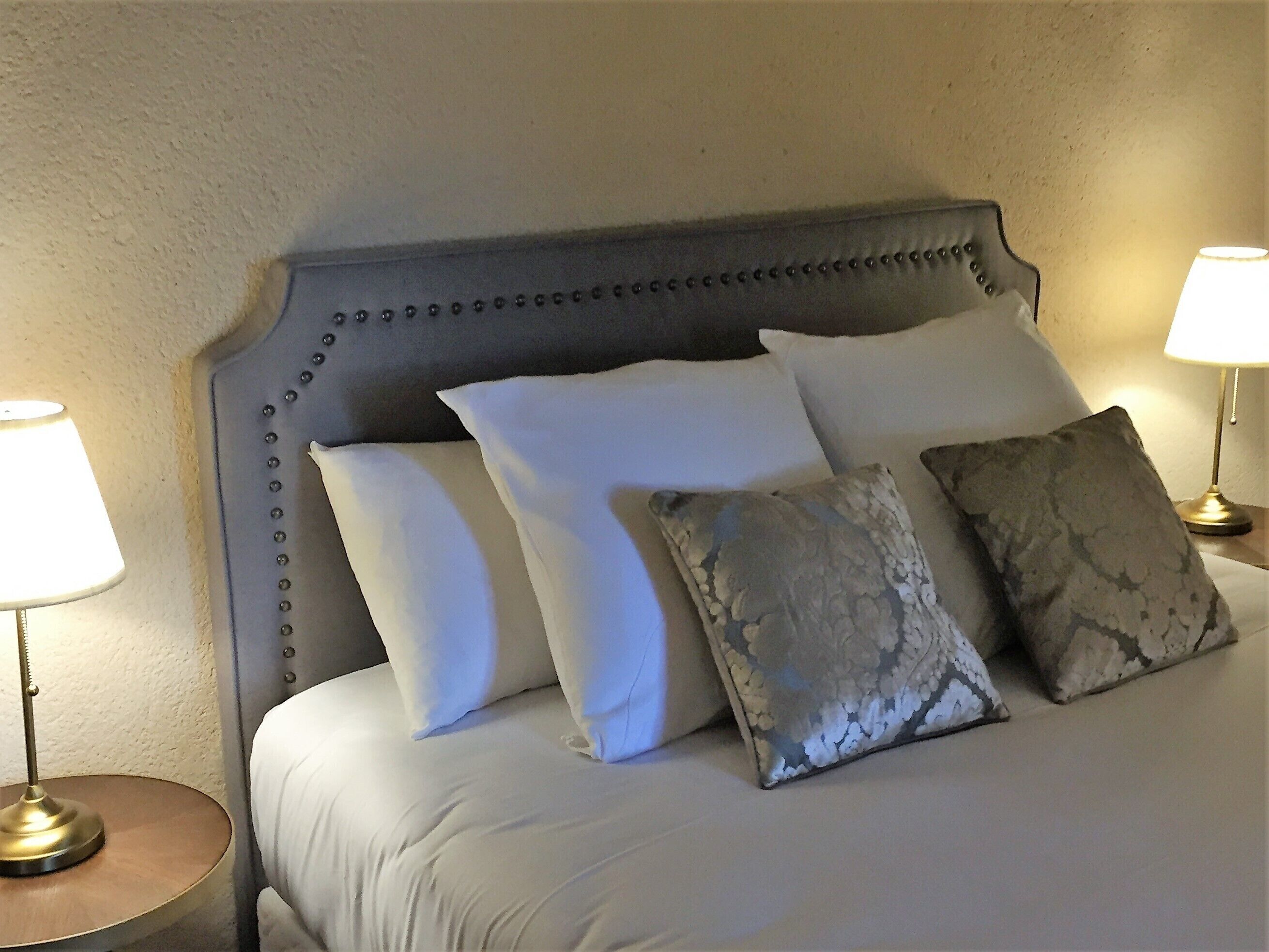 A bed with a tufted headboard, white and patterned pillows, and two bedside lamps on either side.
