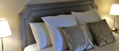 A bed with a tufted headboard, white and patterned pillows, and two bedside lamps on either side.