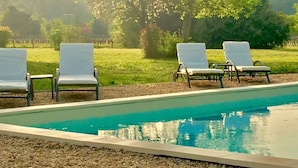 Ett område vid poolen med fyra solstolar och en klarblå pool.