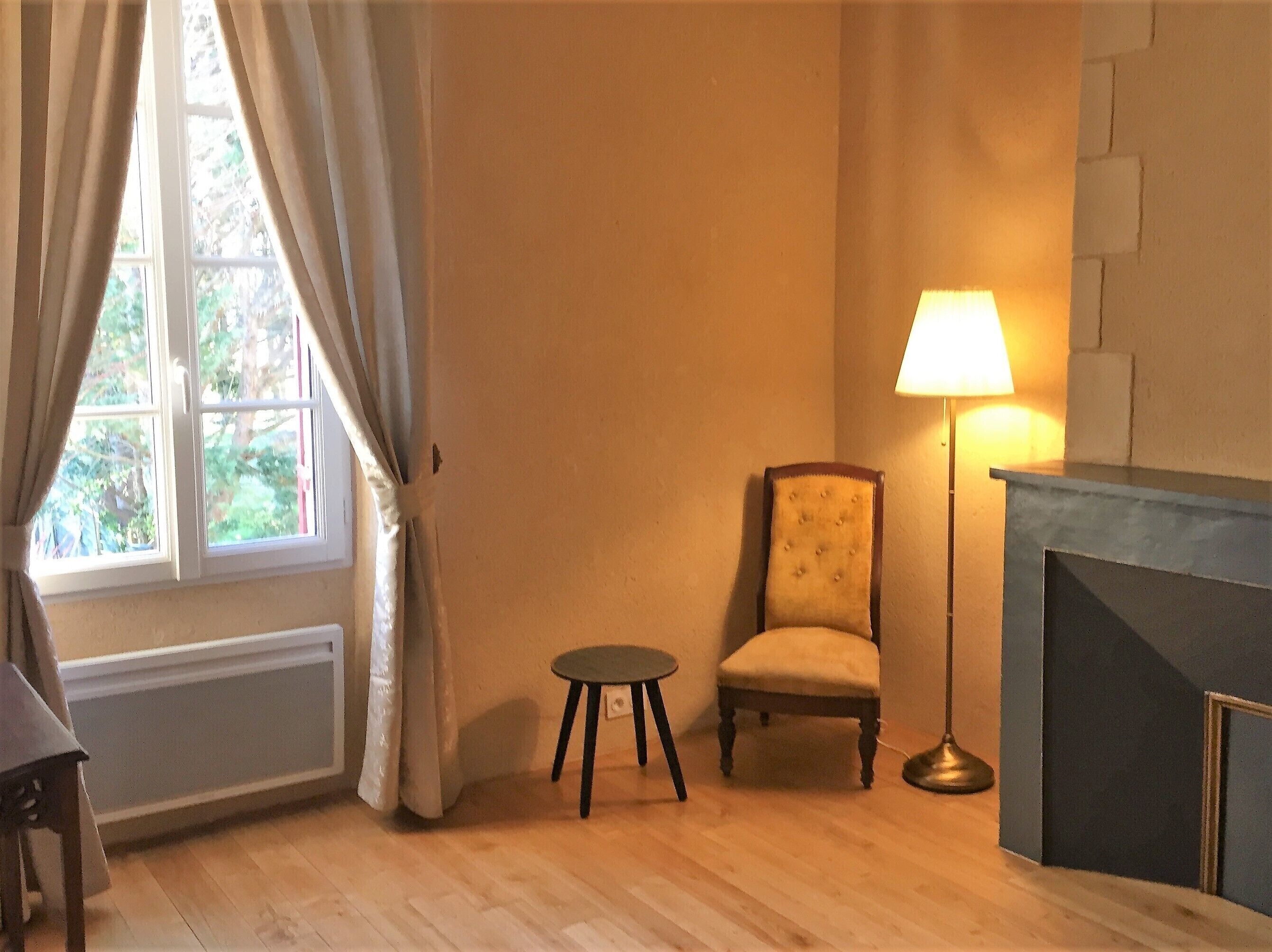 A room with a window, a chair, a small table, and a floor lamp.