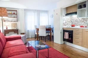 A compact living space with a sofa, dining table, chairs, a kitchen area with a stove and cabinets, and a window with curtains.