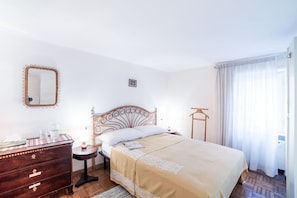 A bedroom with a bed, dresser, nightstand, mirror, and a window with curtains.