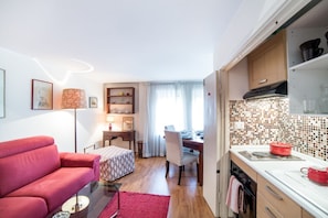 A compact living space with a kitchenette, a dining area, and a red sofa.