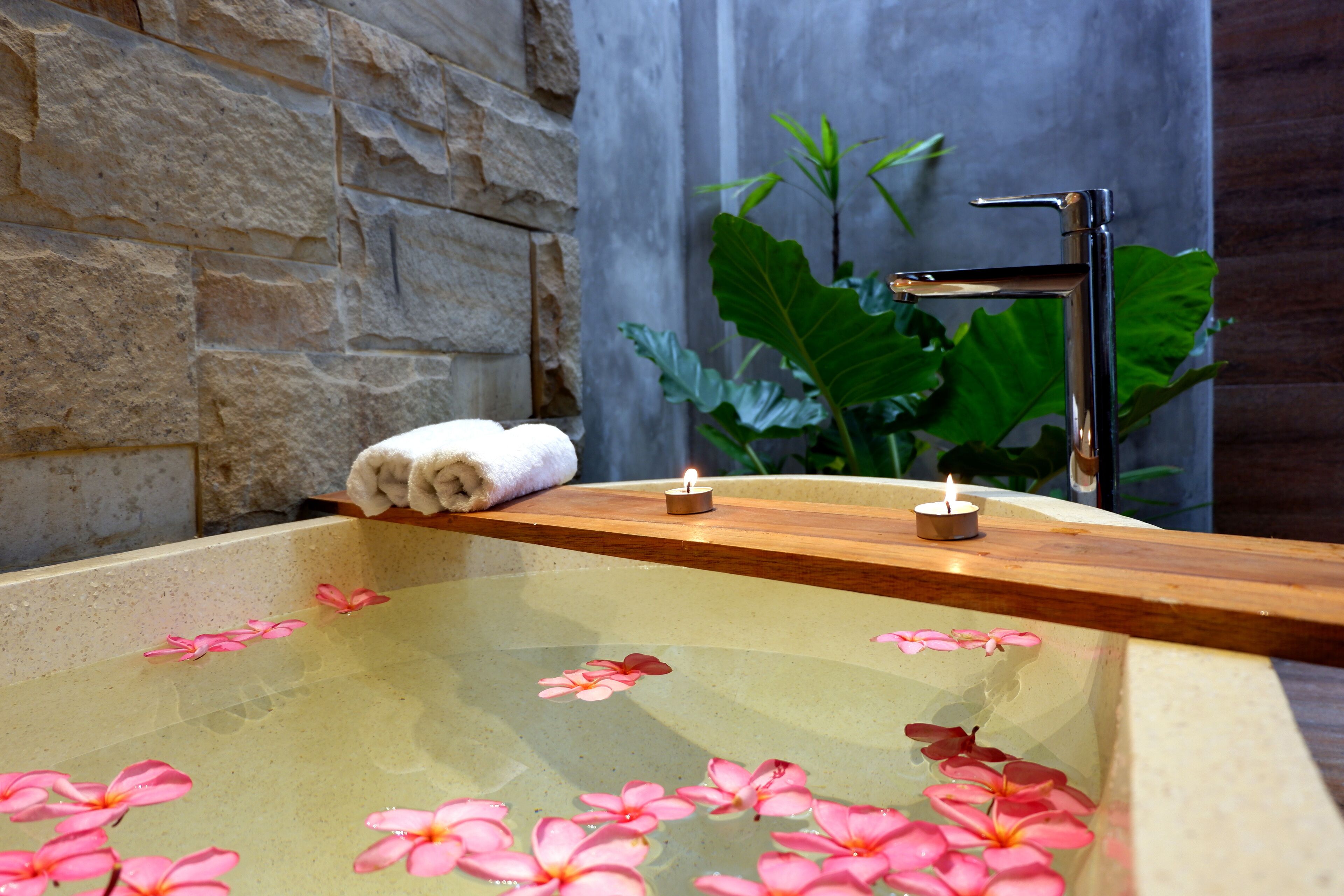 A spa bathtub with pink flowers, a towel, and a candle.