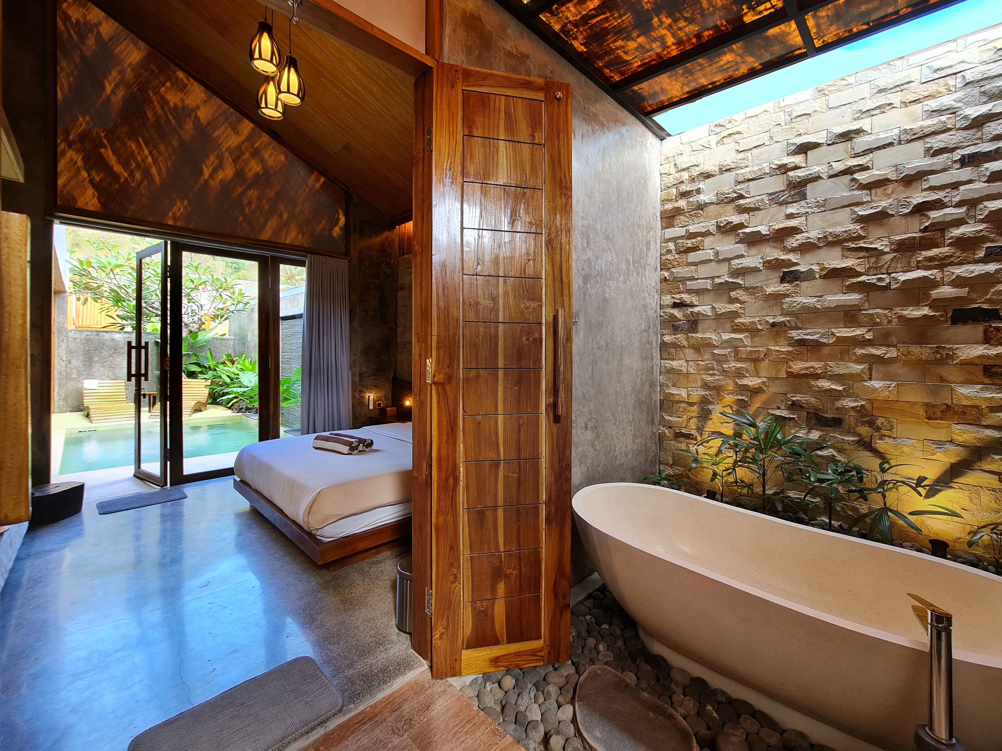 Une salle de bain moderne avec une baignoire sur pieds, une porte en bois et un mur en pierre.