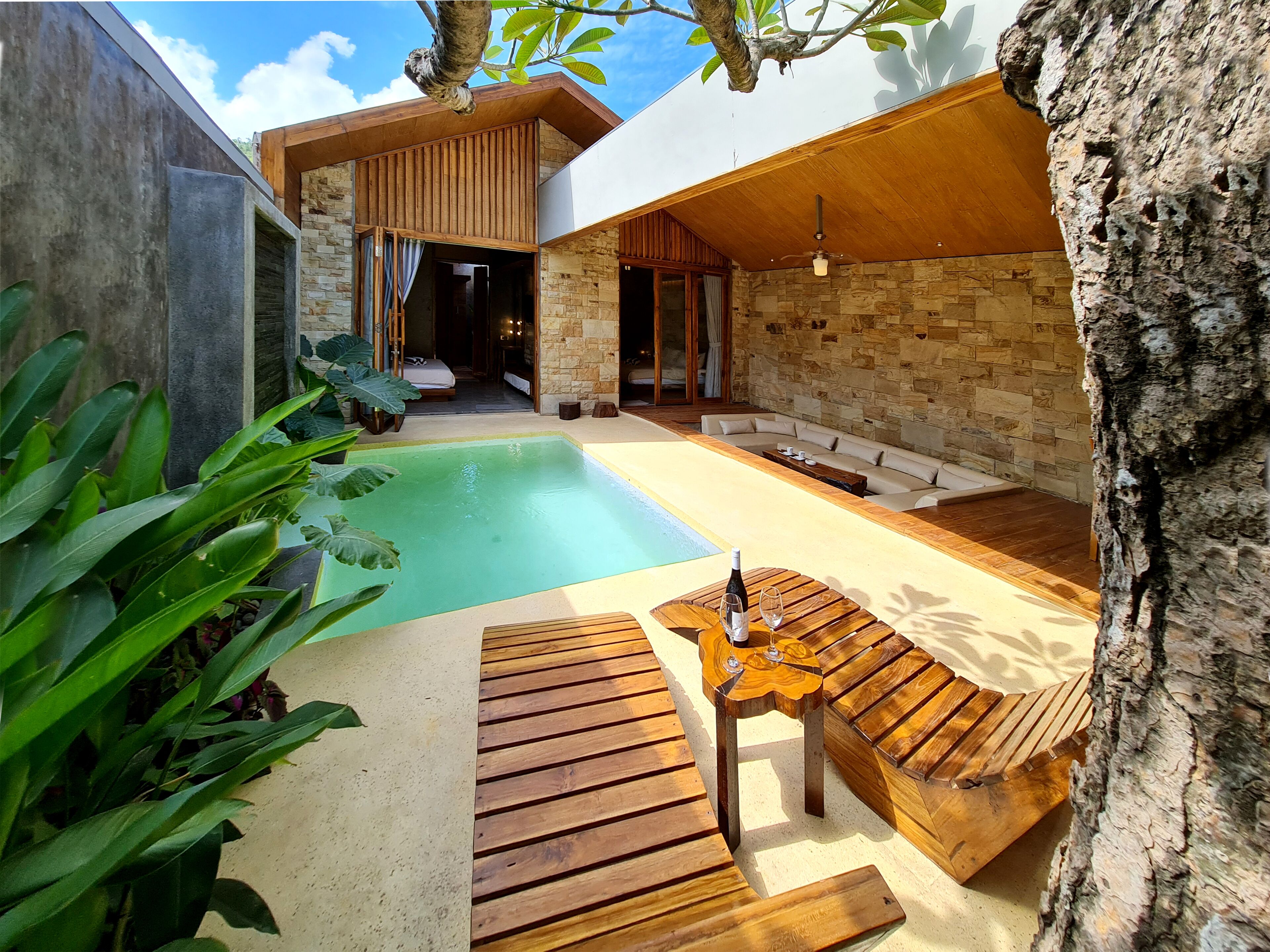 A modern outdoor pool area with a wooden deck, seating, and a table with a bottle and glasses.