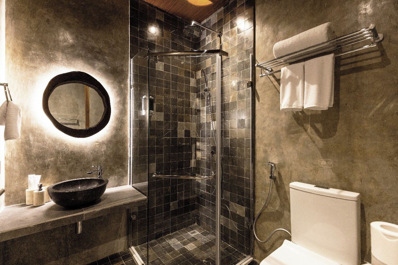 A modern bathroom with a glass-enclosed shower, a round mirror, a black sink, and a towel rack with towels.
