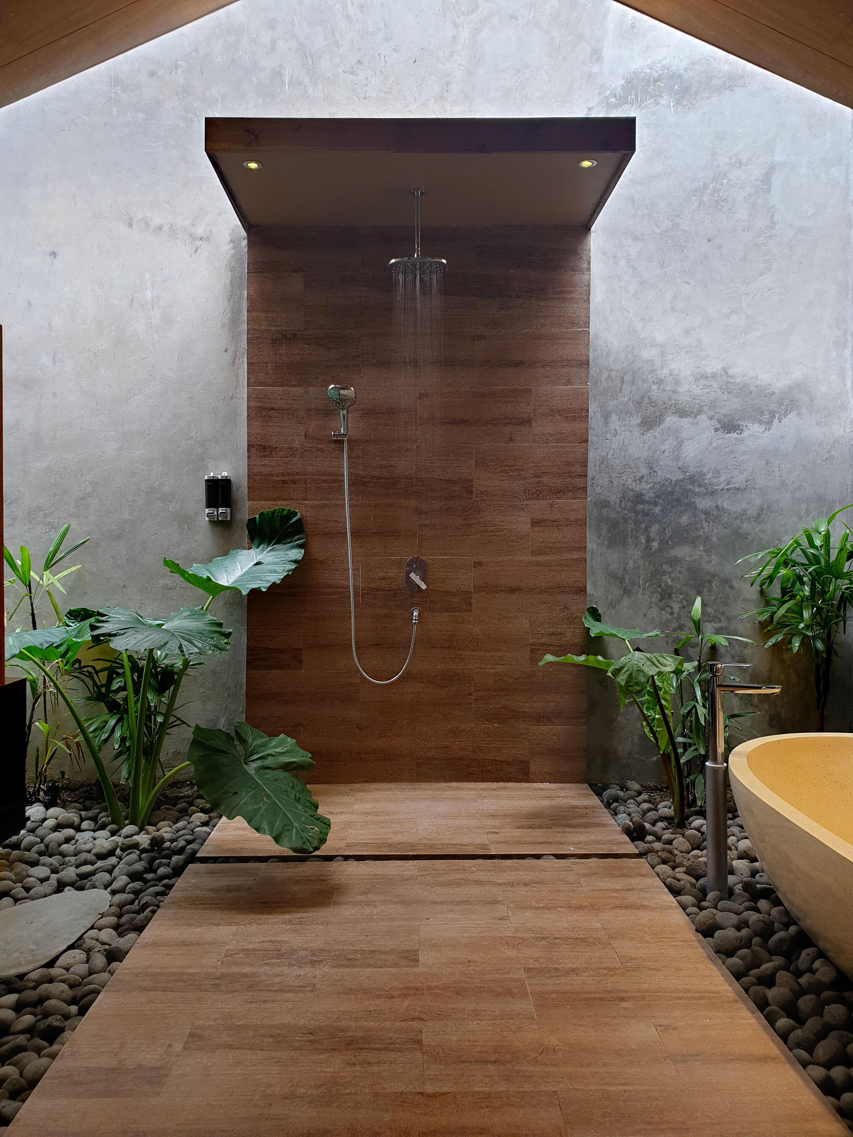 Un área de ducha moderna con pared de paneles de madera, un cabezal de ducha de mano y una bañera.