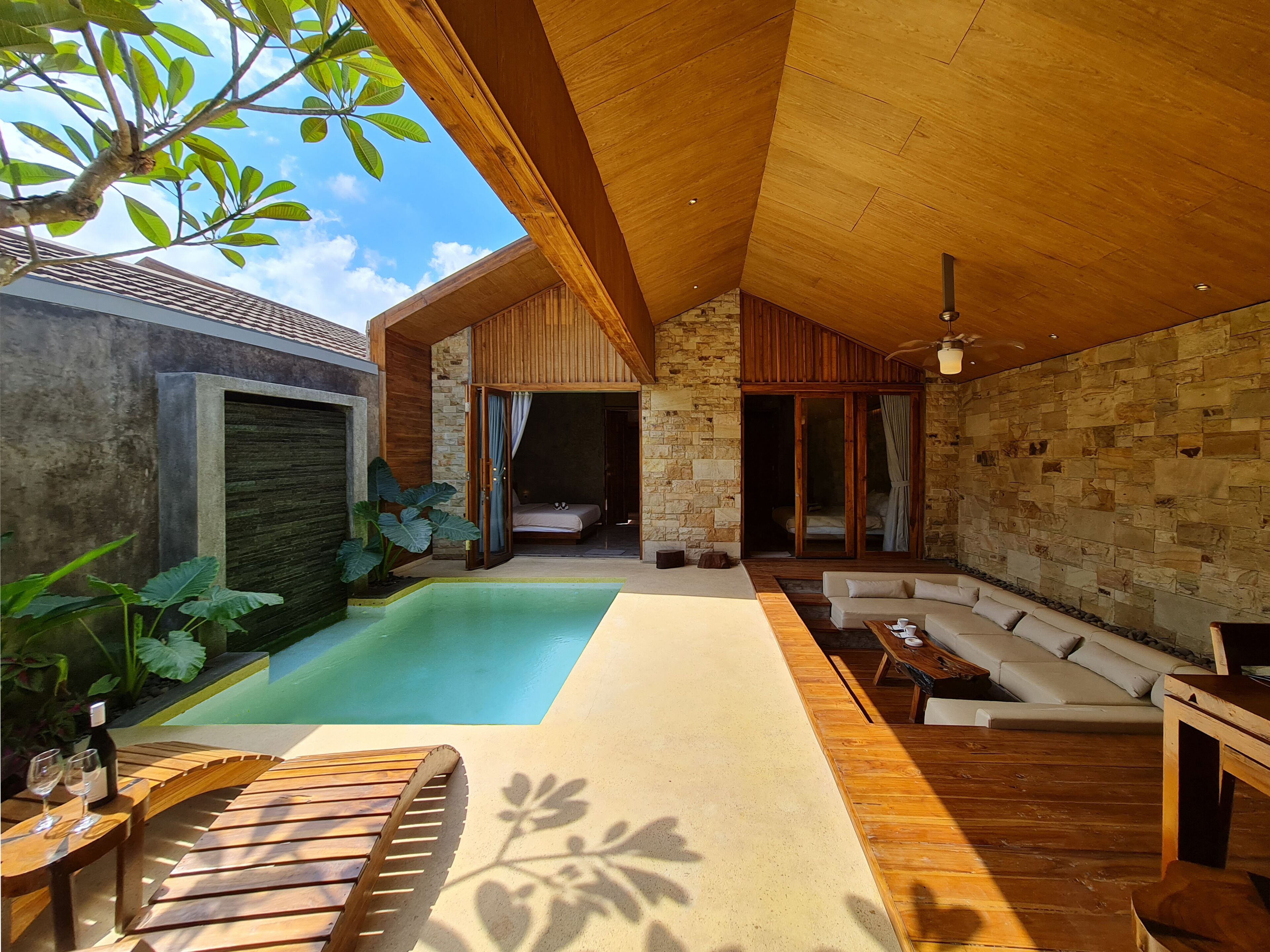 A modern outdoor living area with a pool, wooden furniture, and a stone wall.