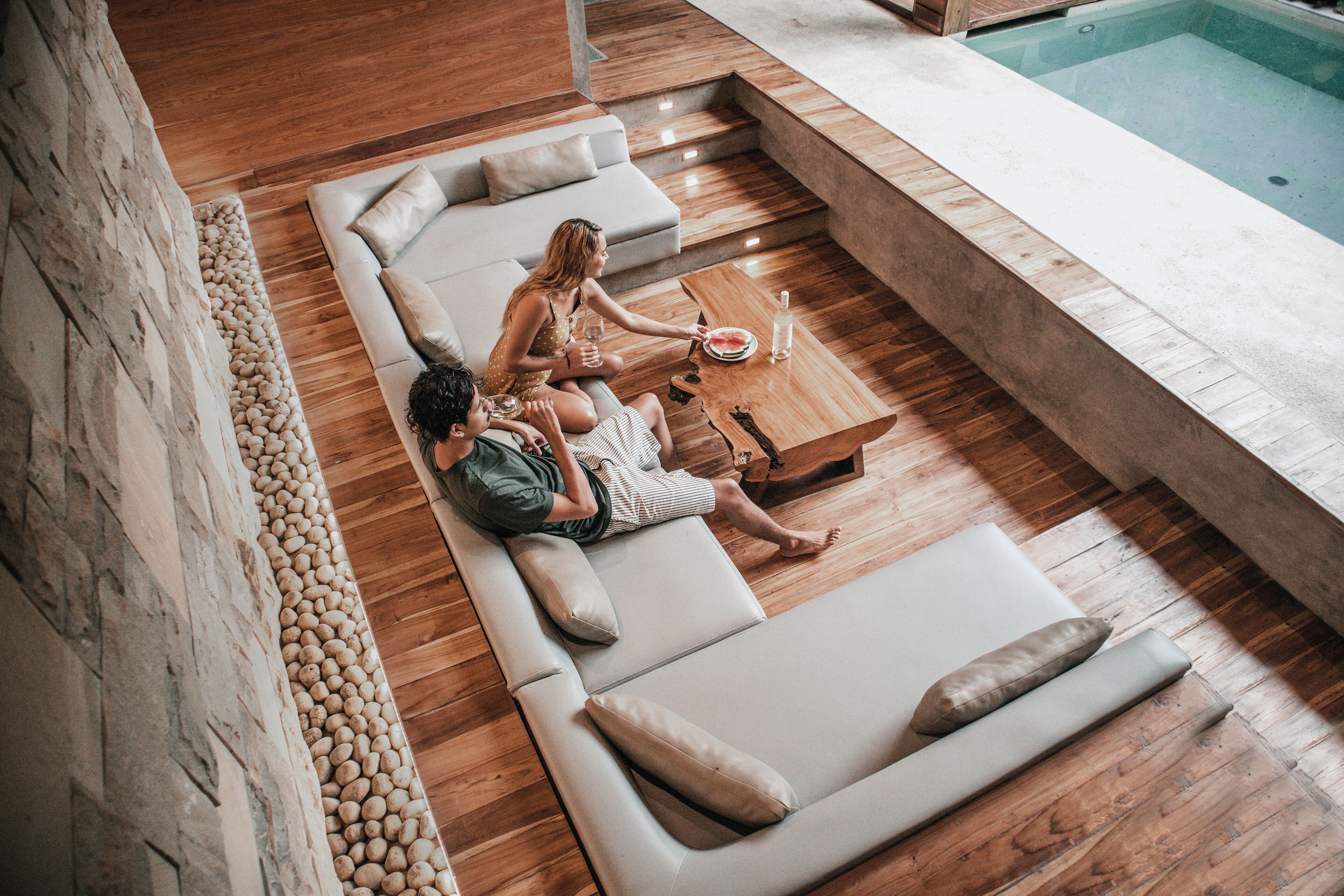 A modern lounge area with a pool, wooden flooring, and a stone wall.