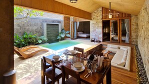 A modern outdoor dining area with a pool, wooden furniture, and a stone wall.