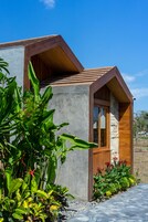 A modern house with a stone exterior, wooden accents, and a garden with tropical plants.