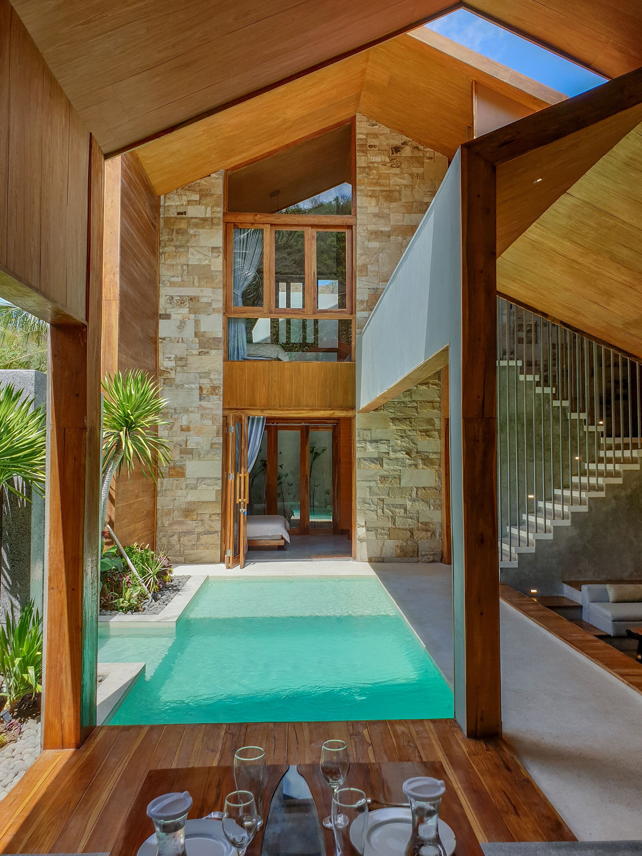A modern villa with a pool, wooden deck, and a staircase leading to a second floor.