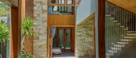 A modern villa with a pool, wooden deck, and a staircase leading to a second floor.