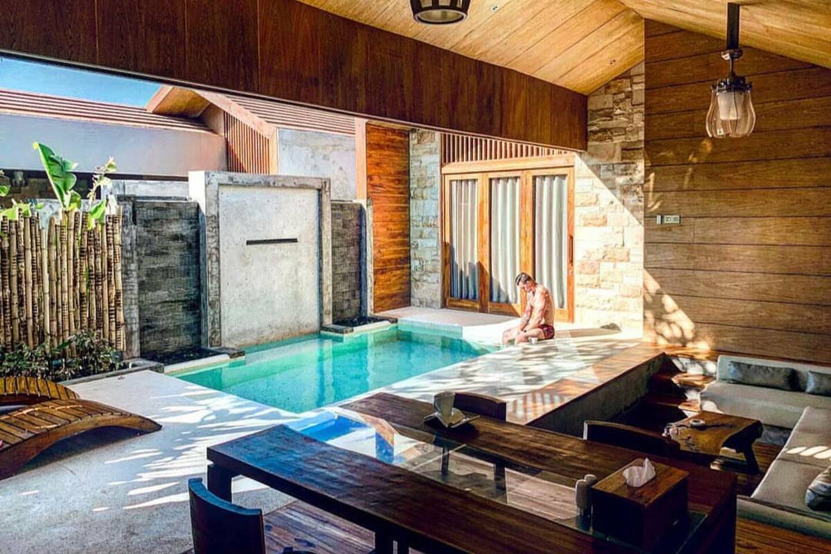 A modern outdoor pool area with a stone wall, wooden deck, and a person sitting by the pool.