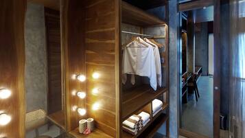 A room with a vanity area featuring a mirror with lights, a chair, and a table with a towel and a cup.