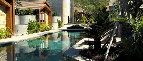 A pool area with clear water, lounge chairs, and a stone building with wooden accents.