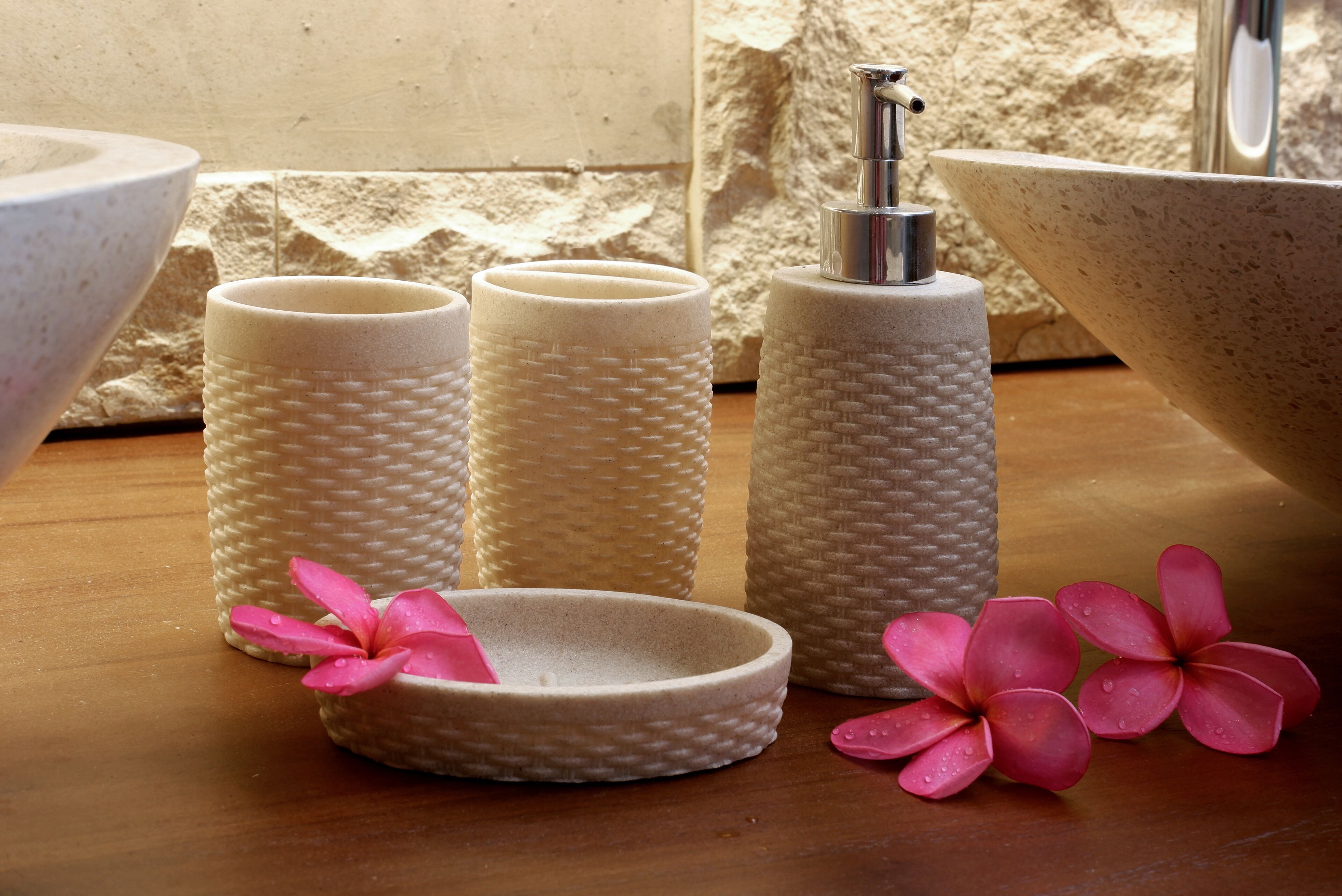 A bathroom with a large bowl sink, three textured soap dispensers, a small bowl, and two pink flowers.