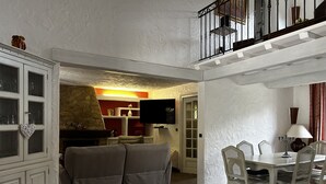 A living room with a sofa, a dining table with chairs, a staircase, and a television.