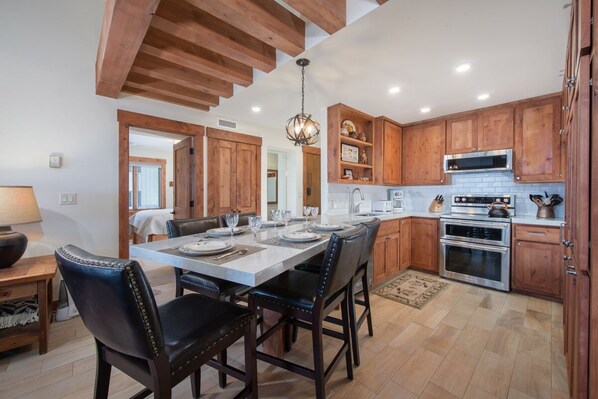 A kitchen with wooden cabinets, a central island with seating, a built-in oven, and a hanging light fixture.