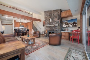 A spacious living area with a fireplace, wooden furniture, and a kitchen in the background.