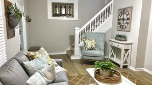 A living room with a grey sofa, a white coffee table with a plant, a blue armchair, a staircase, and a white console table with a plant. - Urban Oasis 3 Miles to Cincy Sleeps 12 (Dayton)