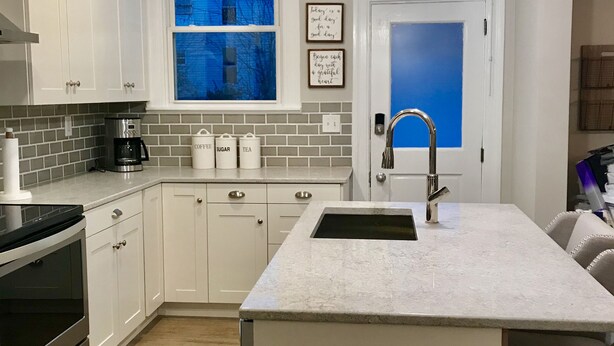 A modern kitchen with white cabinetry, a large island with a sink, a coffee maker, and a window with a view of a blue building. - Urban Oasis 3 Miles to Cincy Sleeps 12 (Dayton)