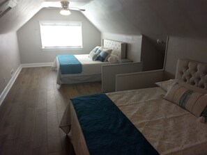 Ett sovrum med ett sluttande tak, en säng med en sänggavel, ett fönster med persienner och en takfläkt.