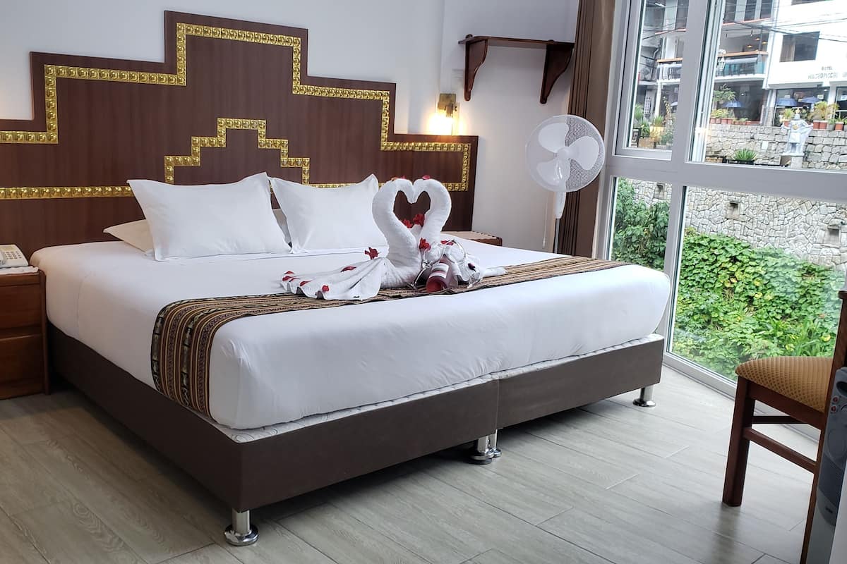 Habitación de hotel con una cama grande, una mesita de noche con teléfono, una lámpara de pared y vistas a zonas verdes.