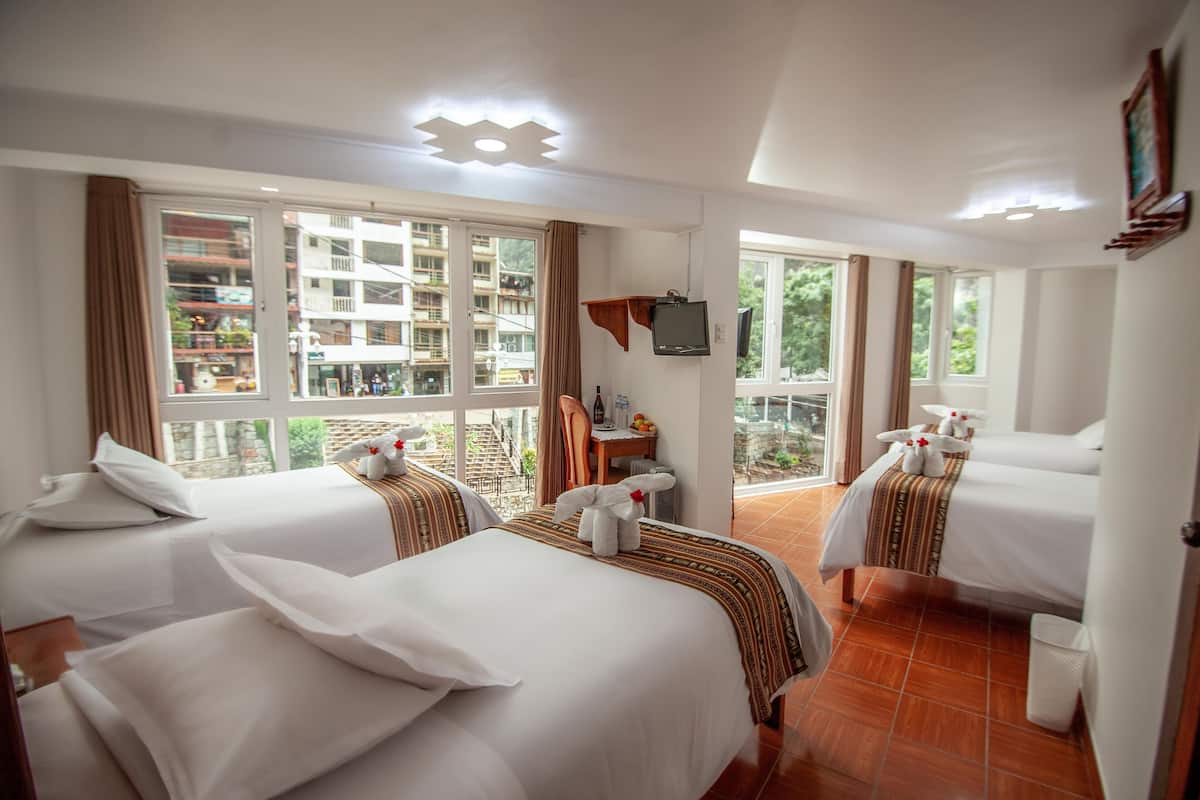 Habitación de hotel con dos camas, televisión y balcón con vistas a edificios.