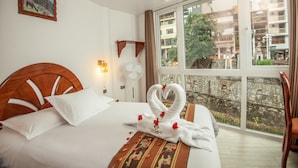 A hotel room with a large window, a bed with white linens, a wooden headboard, and a decorative towel arrangement. - MAPILAND-Hotel Boutique. a unos pasos de la estación de tren y de autobus. Con vista al río y a las montañas (Machu Picchu)
