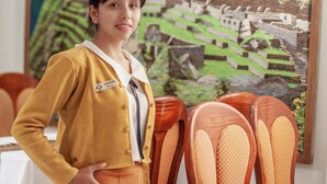A person standing in a dining area with wooden chairs and tables, a large painting on the wall depicting a landscape, and a name tag on the person's jacket. - MAPILAND-Hotel Boutique. a unos pasos de la estación de tren y de autobus. Con vista al río y a las montañas (Machu Picchu)