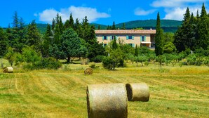 Un bâtiment avec un toit en tuiles, entouré d’arbres et de bottes de foin dans un champ.