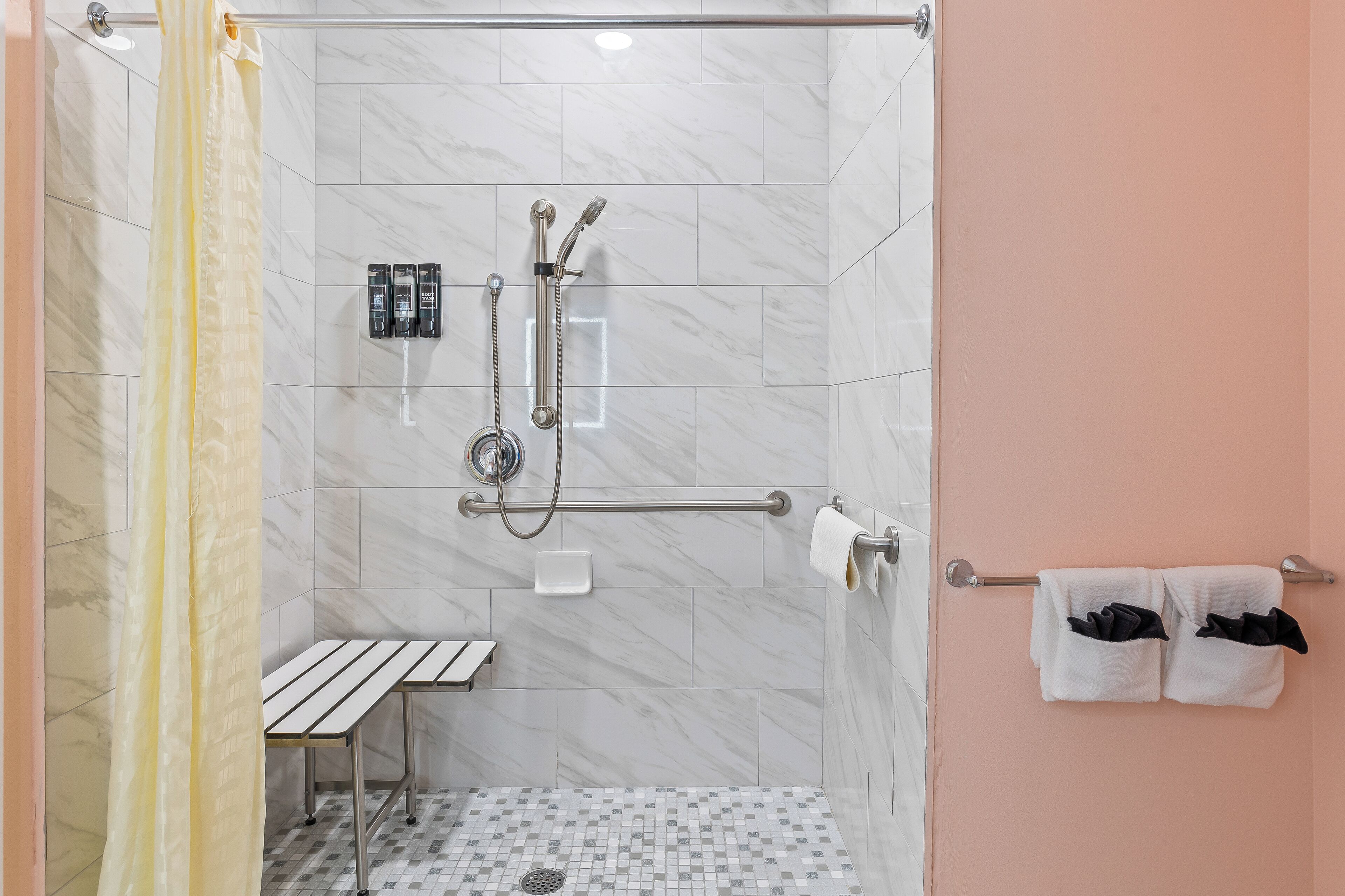 Une douche à l’italienne avec une porte en verre, un banc, un sèche-mains et un porte-serviettes avec des serviettes.