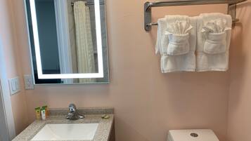A bathroom with a granite sink, a mirror with a light, a towel rack with two towels, a toilet, and a shower curtain.