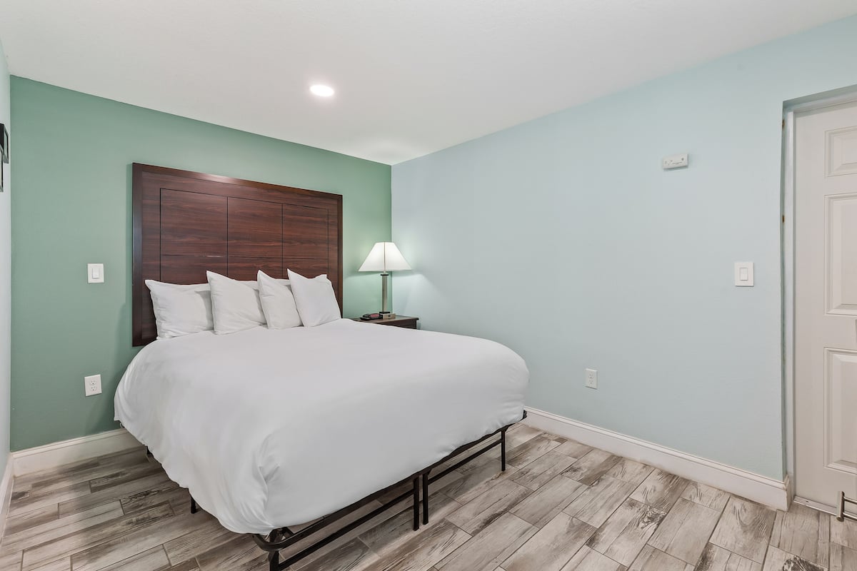 A bedroom with a bed, a nightstand, a lamp, and a door.