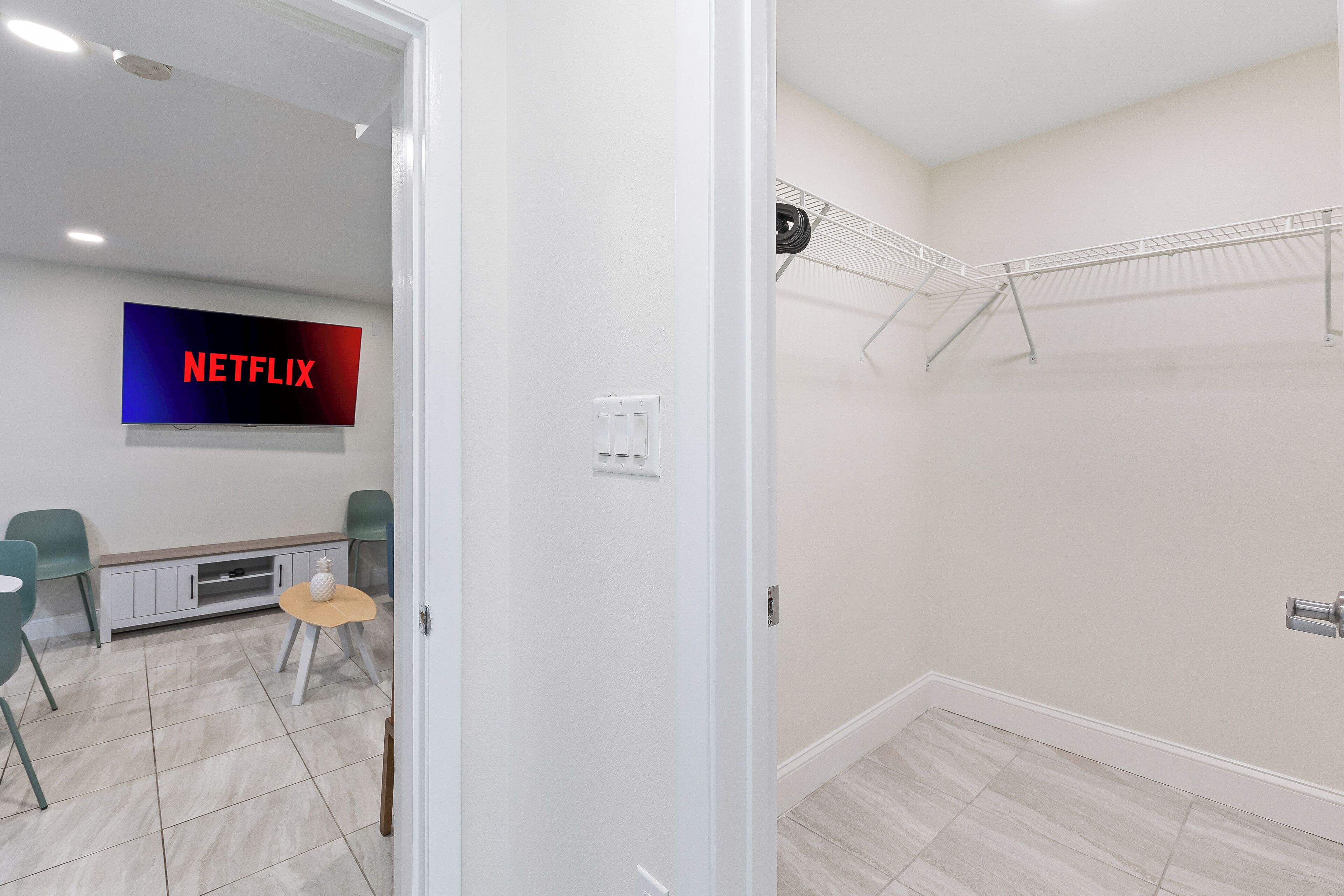 Ein Zimmer mit Fernseher, auf dem 'NETFLIX' zu sehen ist, einem kleinen Tisch mit einer Ananas und einem Wäscheständer.