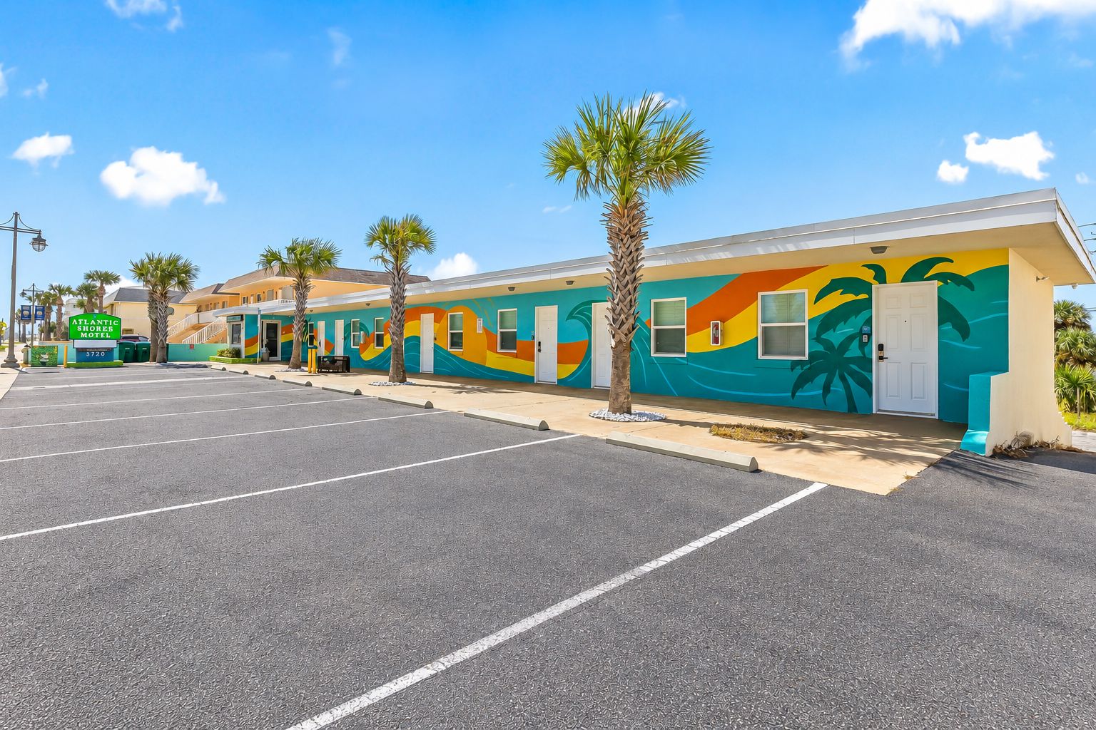 A motel with a colorful mural, a parking lot, and palm trees.