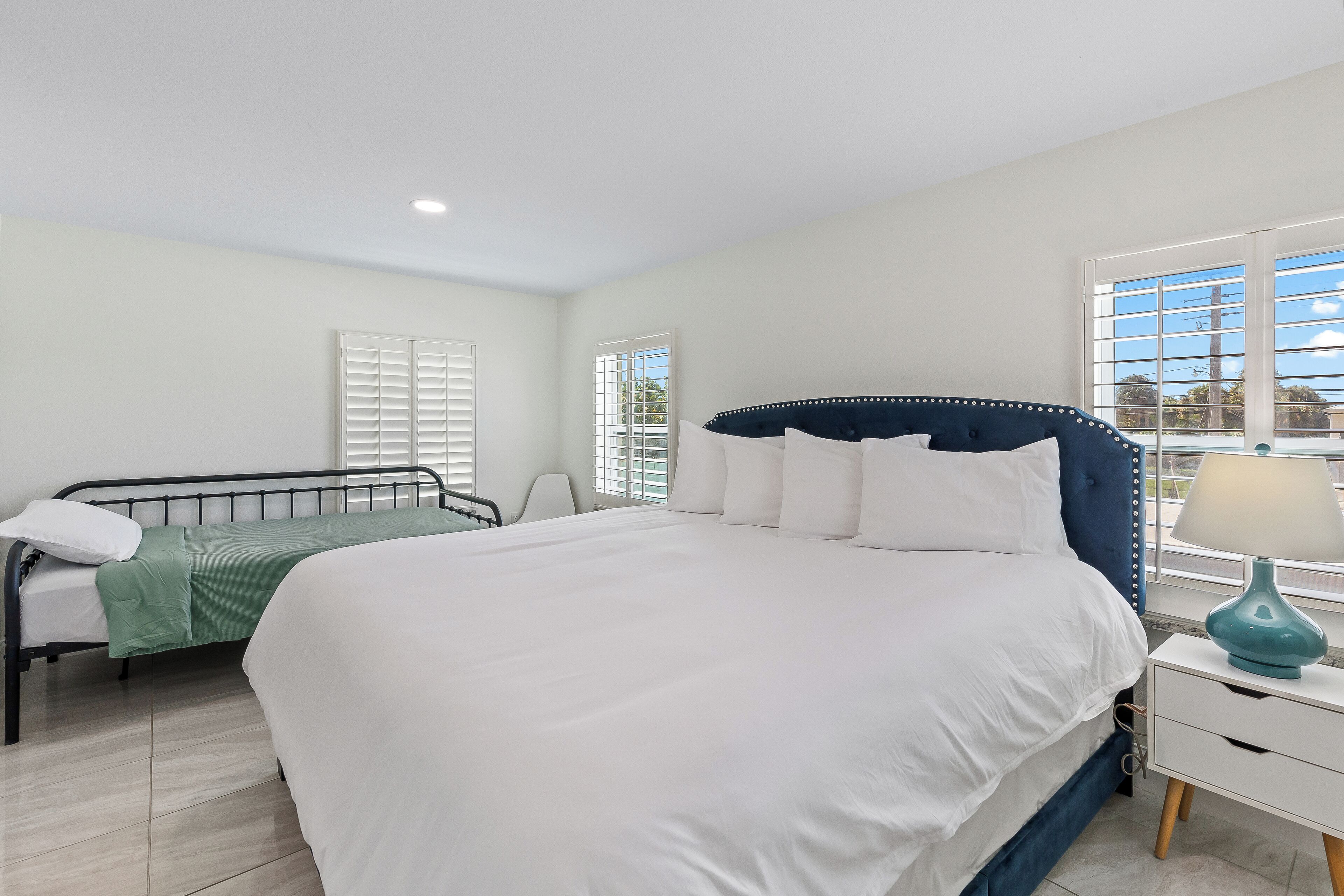 A bedroom with a large bed, a smaller bed, a nightstand, and a window with blinds.