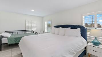 A bedroom with a large bed, a smaller bed, a nightstand, and a window with blinds.
