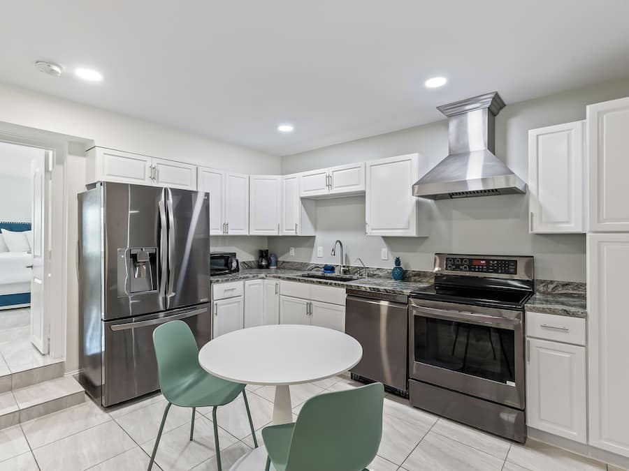 Una cocina moderna con electrodomésticos de acero inoxidable, armarios blancos y una mesa de comedor redonda con dos sillas.
