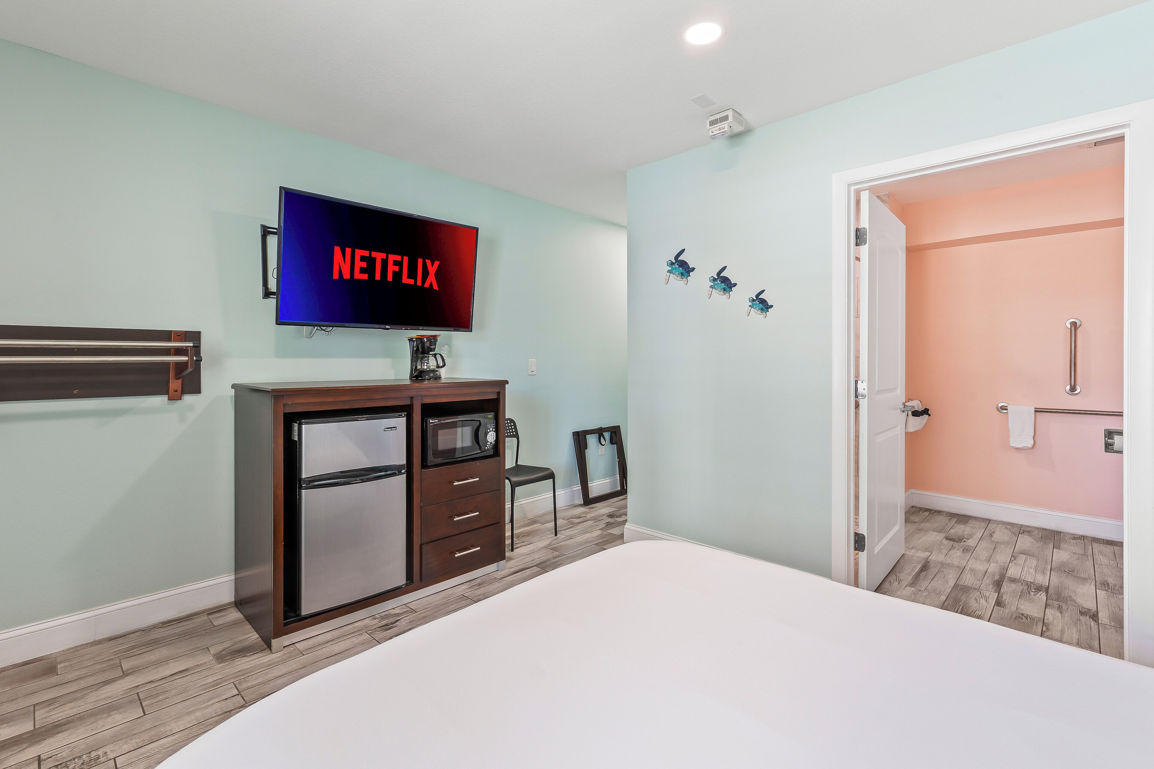 A bedroom with a bed, a TV mounted on the wall, a dresser, and a door leading to a bathroom.